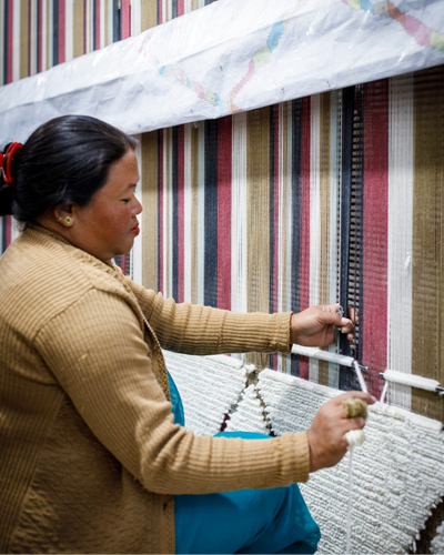 Woman operating a loom with colorful striped fabric in the background