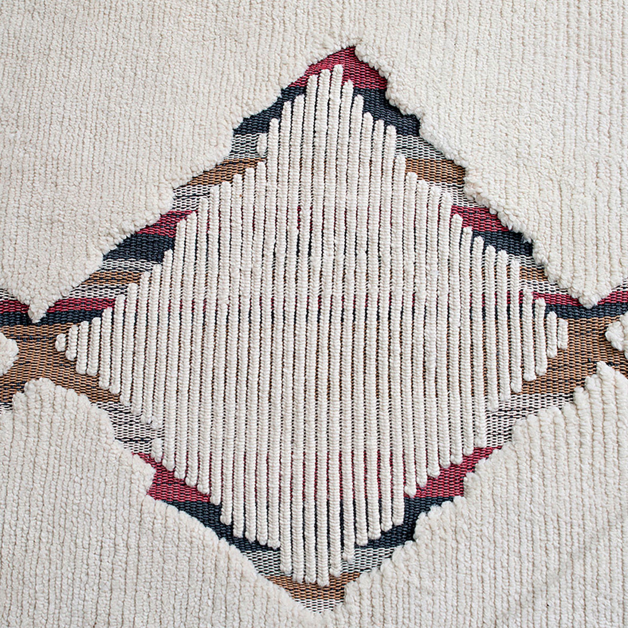 Close-up view of a textured rug with a geometric pattern featuring beige, red, and blue colors.